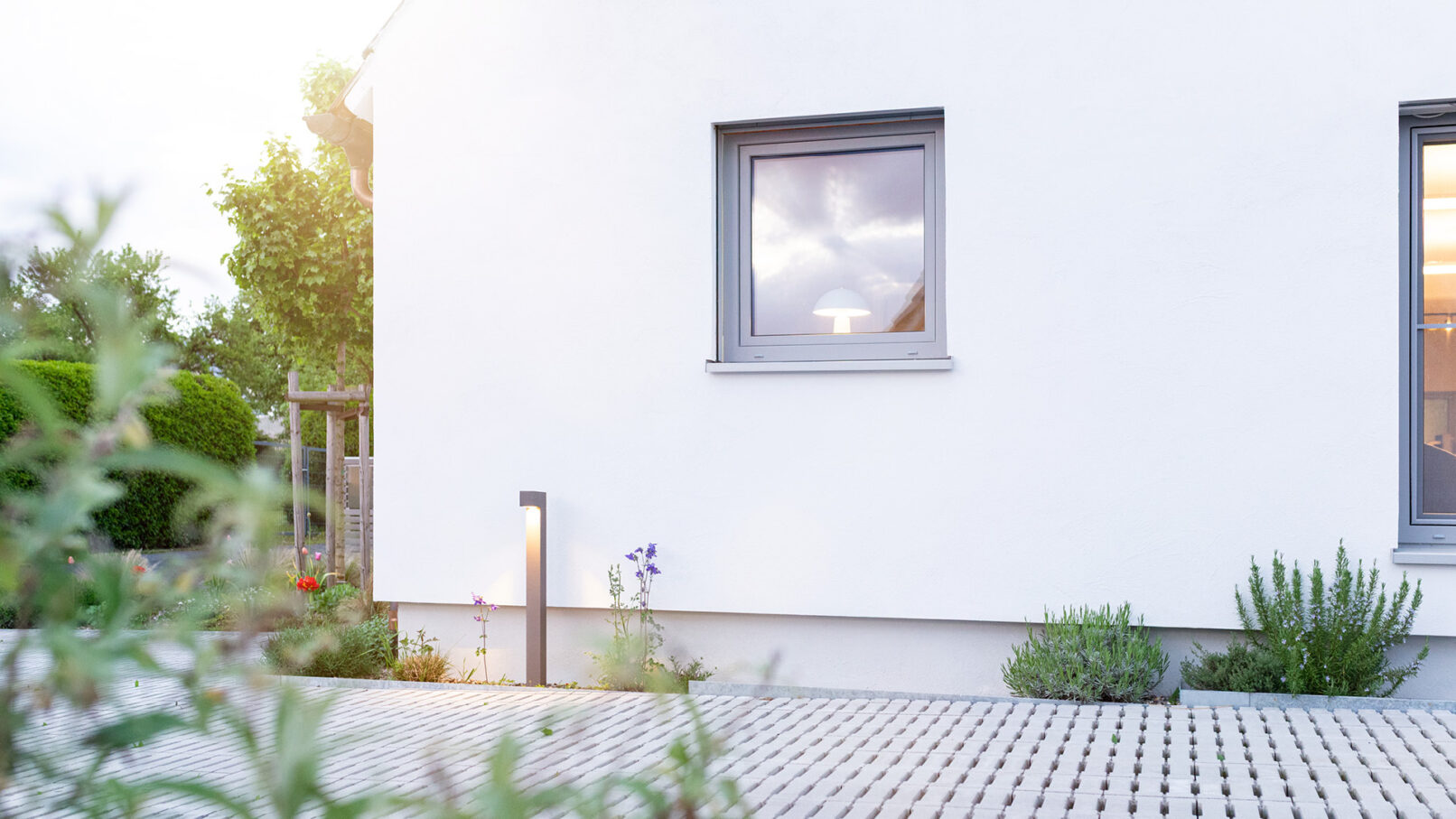 Modernisierte Fassadengestaltung eines Wohnhauses bei Abenddämmerung mit klar strukturierter Zufahrt und integrierten Pollerleuchten.