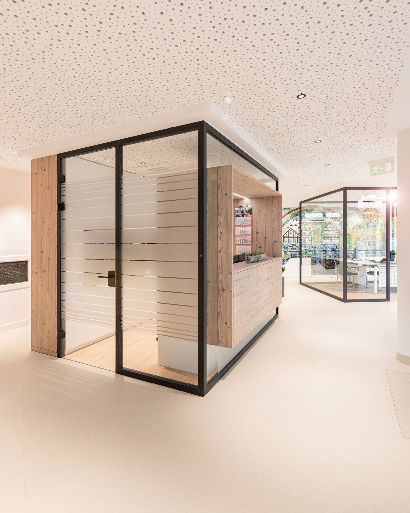 Eingangsbereich RH Wasser Dörth mit Empfangsarbeitsplatz in Glasbox und transparentem Besprechungsraum im Hintergrund