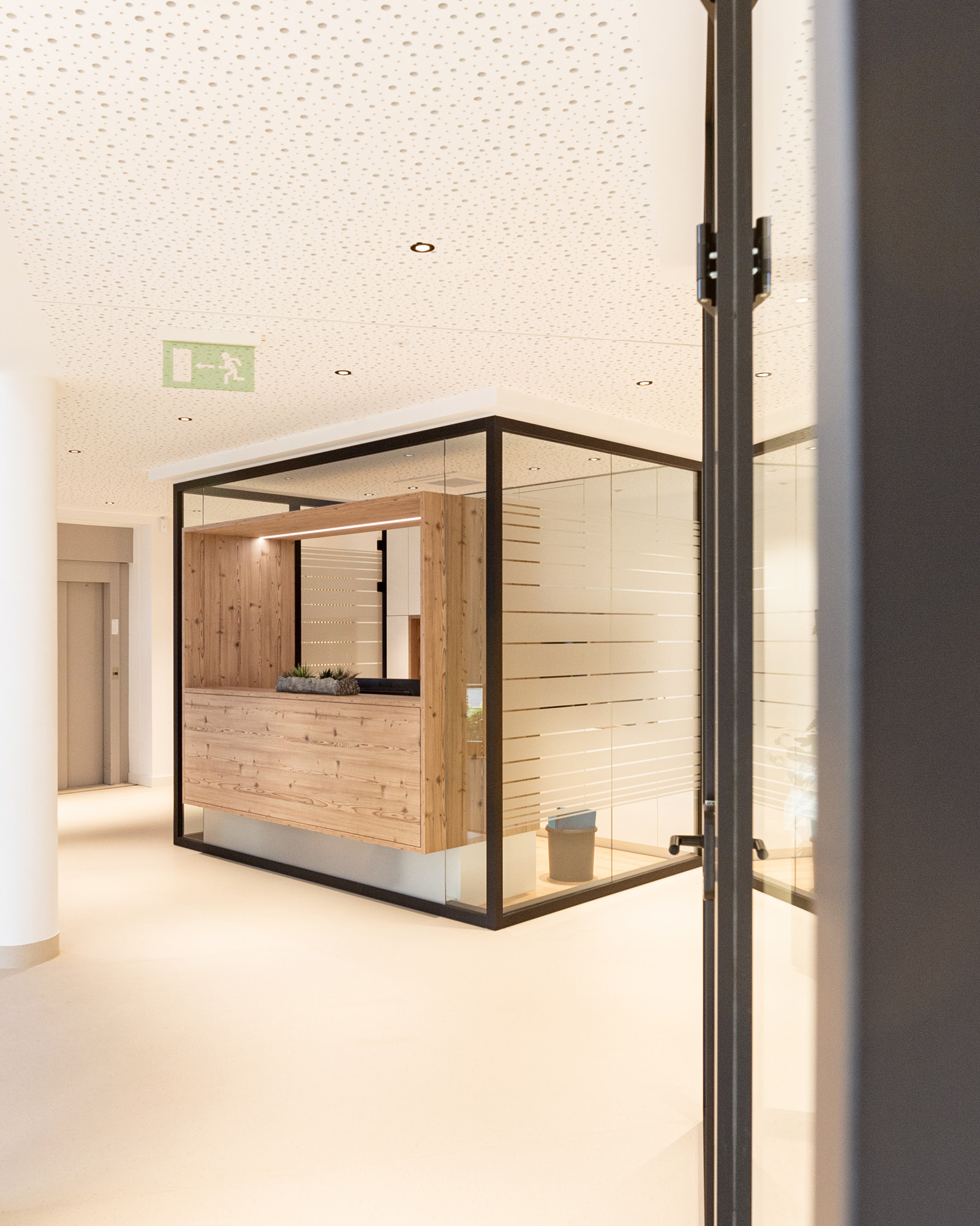 Empfangskubus im Eingangsbereich RH Wasser Dörth mit Holzverkleidung, Glaswänden und integriertem Arbeitsplatz